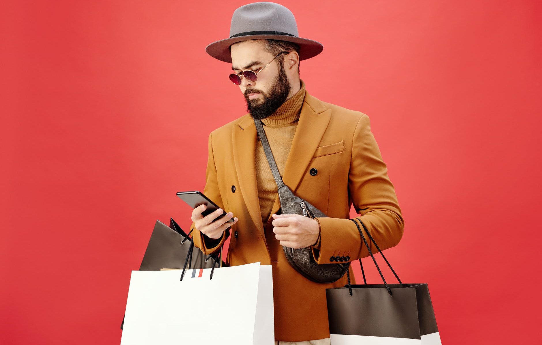 man in a brown blazer carrying shopping bags while using his cell phone