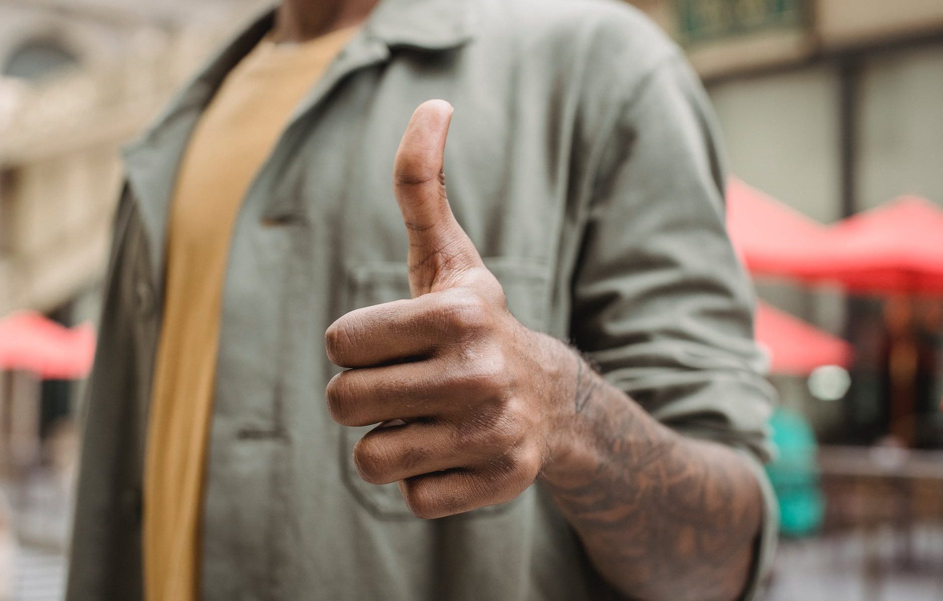 anonymous ethnic man demonstrating thumb up sign on street