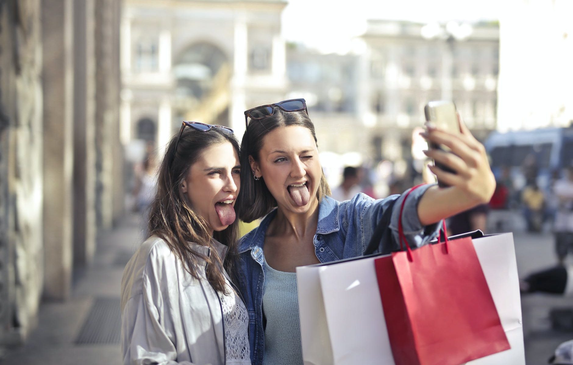 cheerful young women with shopping bags taking selfie on street
