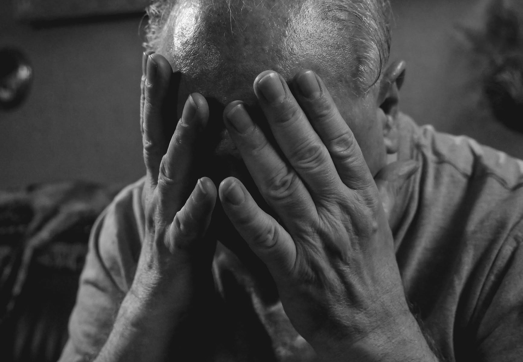a grayscale photo of an elderly man covering his face