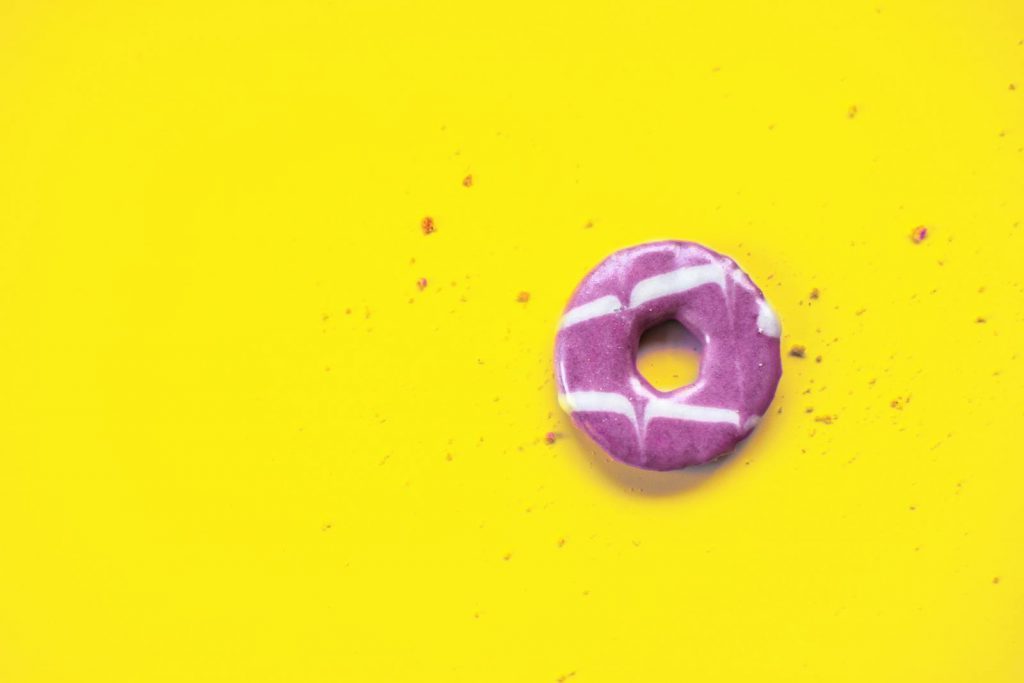 A single purple doughnut with white stripes on a bright yellow backdrop, creating a striking color contrast.
