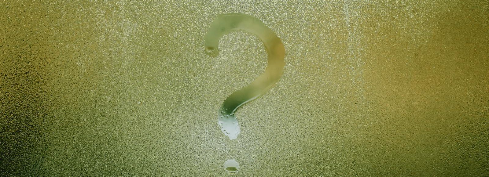 A question mark drawn on foggy glass, evoking curiosity and mystery.