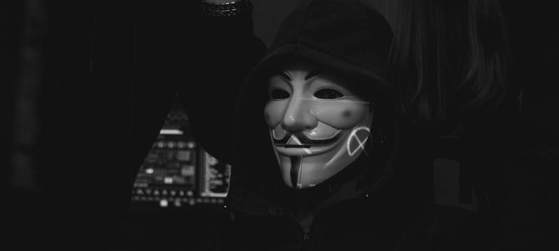A group of hackers wearing Guy Fawkes masks work on computers indoors, symbolizing cybersecurity threats.